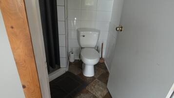 Un baño pequeño con inodoro blanco, cortina de ducha y suelo de baldosas.