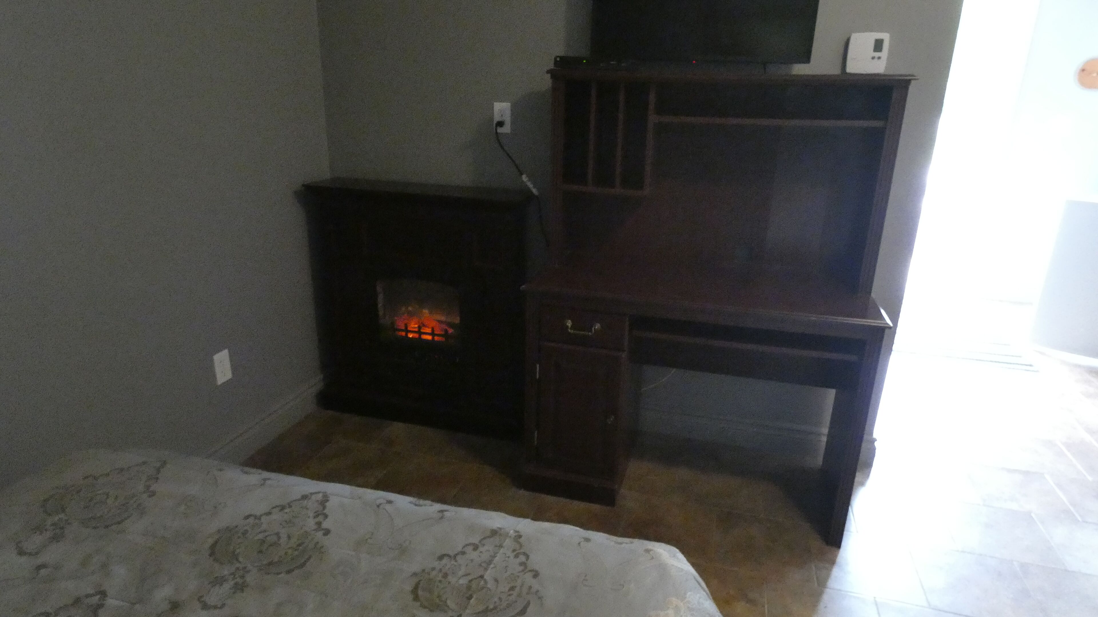 Una habitación con chimenea, televisor en un mueble de madera y colcha estampada.