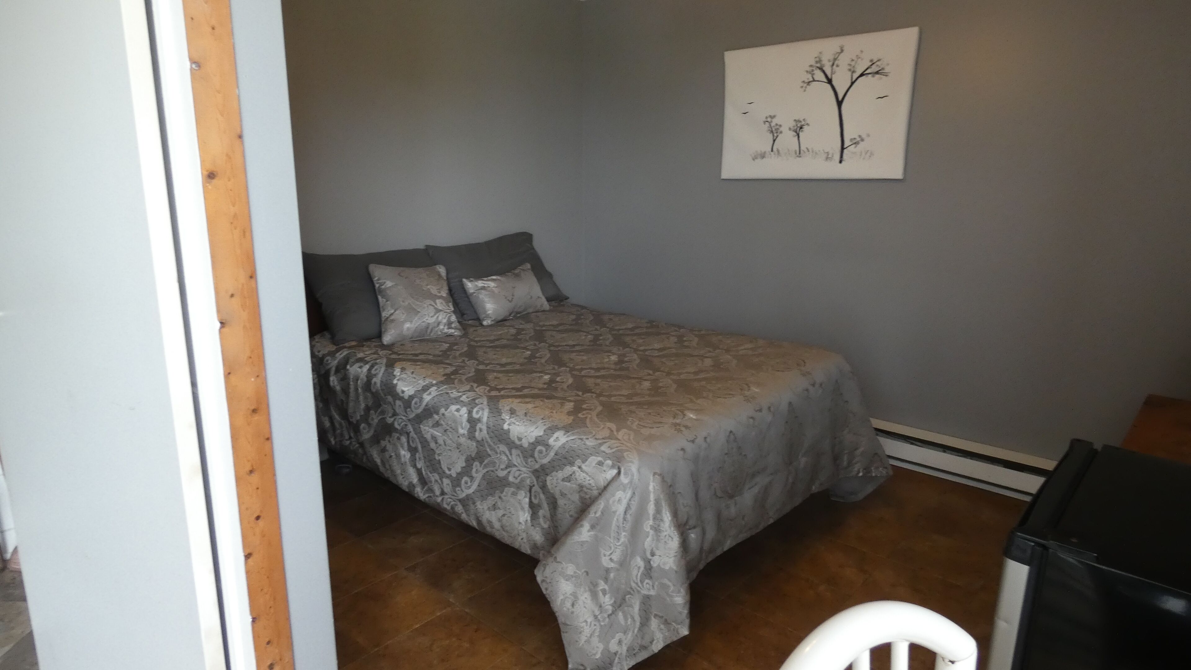 A bedroom with a bed, pillows, a wall-mounted painting, and a trash bin.