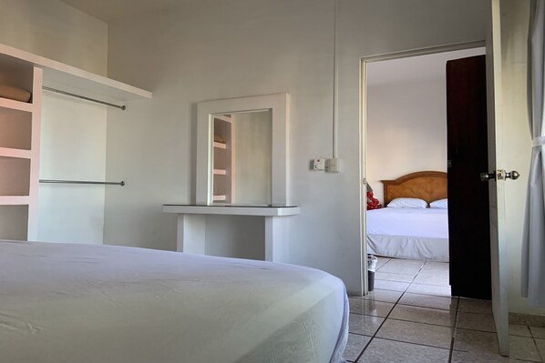 Un dormitorio con una cama, una mesita de noche, un espejo y una puerta abierta que da a otra habitación.