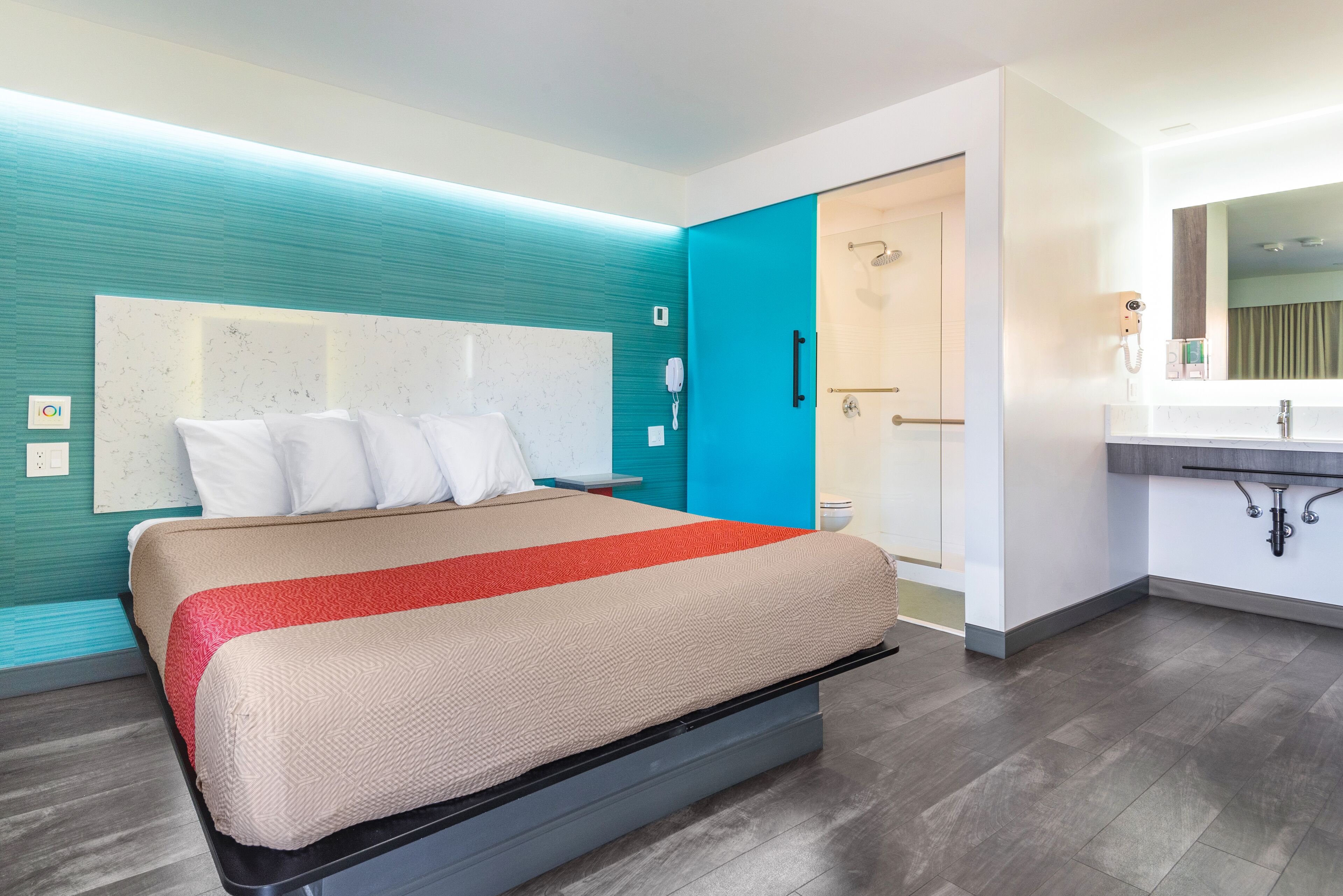 Une chambre d’hôtel moderne avec un grand lit, une salle de bain avec douche et une coiffeuse avec miroir.