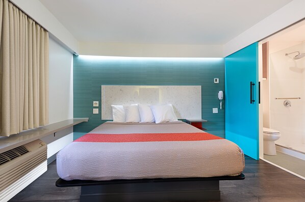 A modern hotel room with a large bed, a built-in heater, a shower area, and a teal accent wall. - Solo Motel - Broadway (Los Angeles)