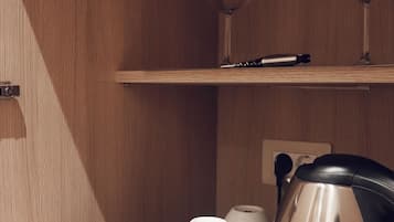 A wooden shelf with a coffee maker, two white cups, a tray with chocolate bars, and two wine glasses.