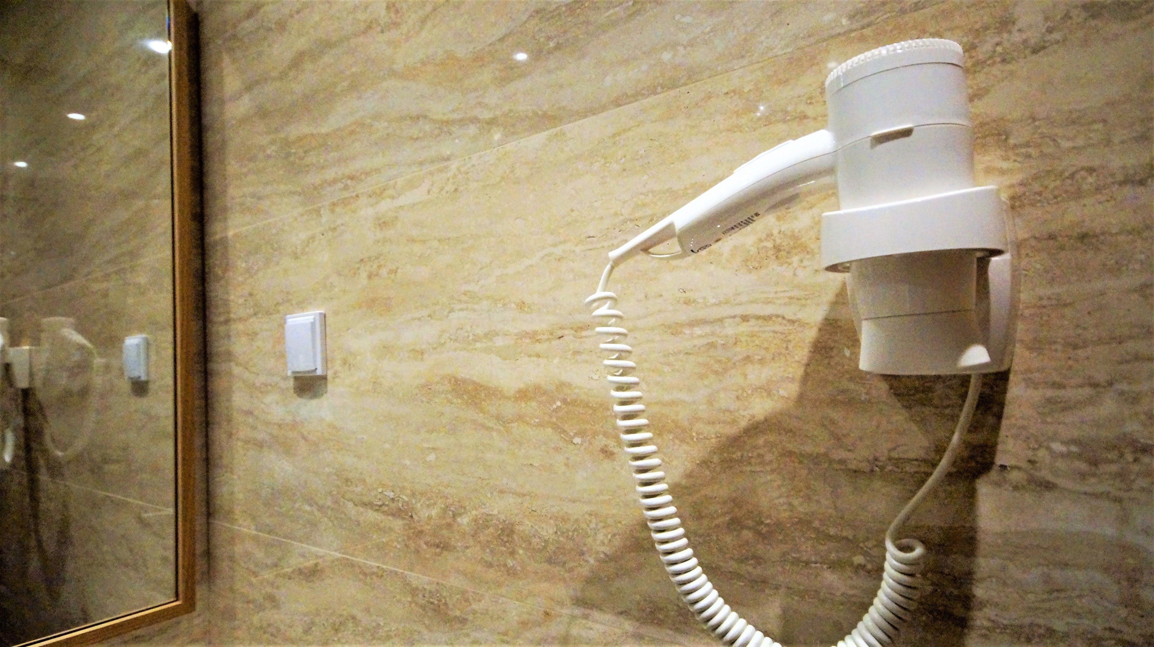 Un sèche-cheveux fixé sur un mur de marbre, un miroir et un interrupteur.