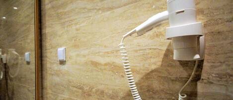 A hair dryer mounted on a marble wall, a mirror, and a light switch.