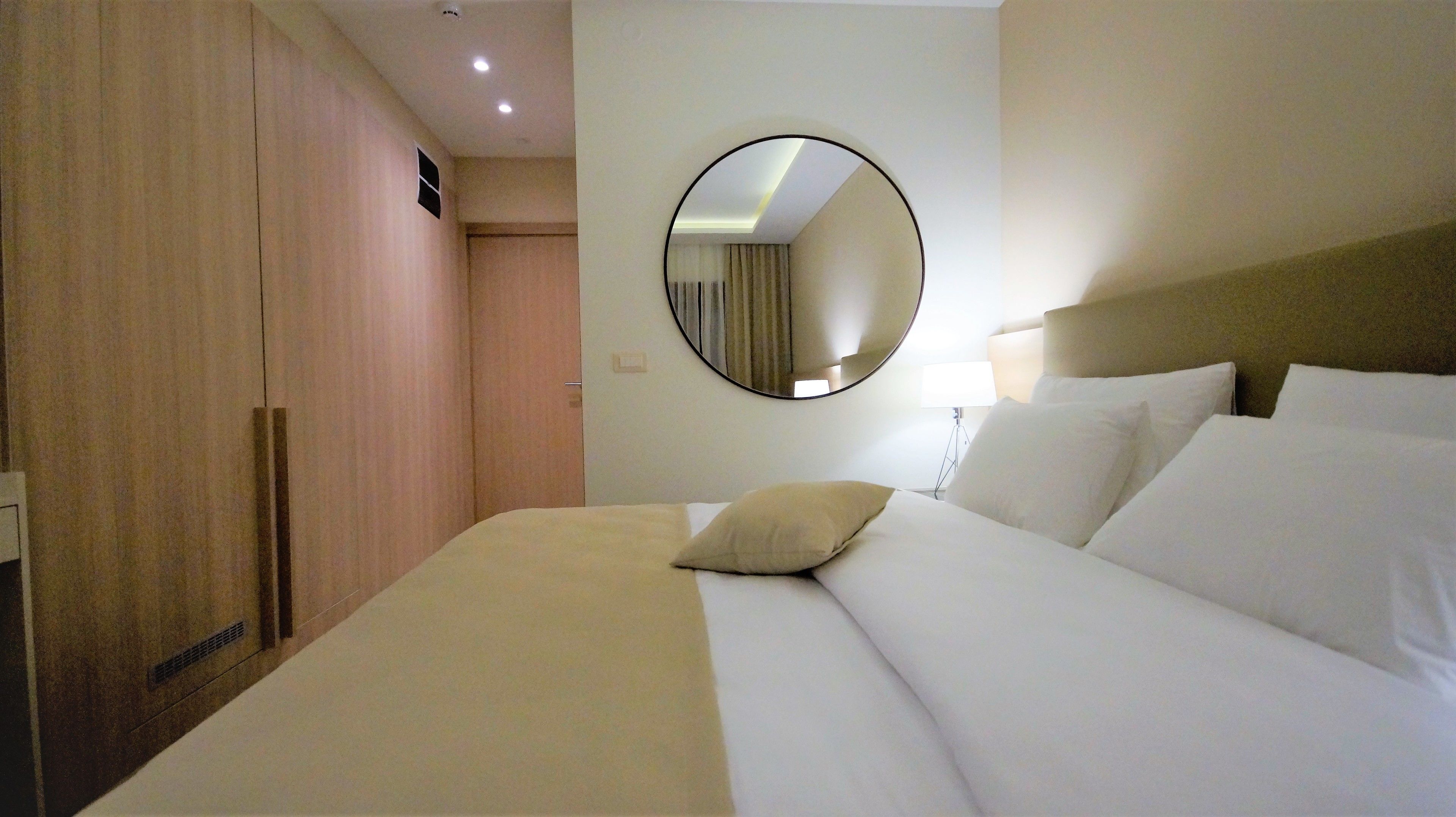 A hotel room with a large bed, a round mirror on the wall, and a wardrobe.
