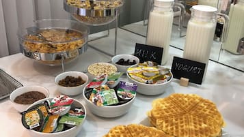 Un bufé con diversas opciones de comida, como waffles, yogur y cereales.