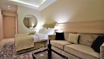 Una habitación de hotel con cama, sofá, espejo redondo, lámpara y botella de vino sobre una mesa.