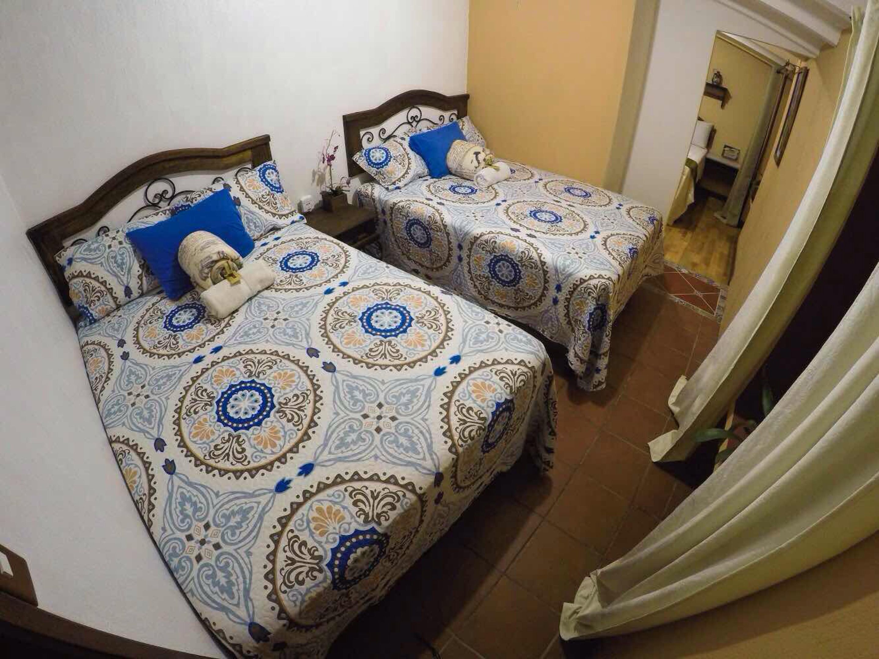 Duas camas de solteiro com roupa de cama estampada, um painel de madeira e uma cortina à direita.
