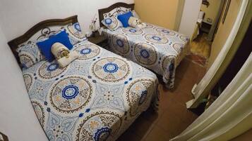 Duas camas de solteiro com roupa de cama estampada, um painel de madeira e uma cortina à direita.