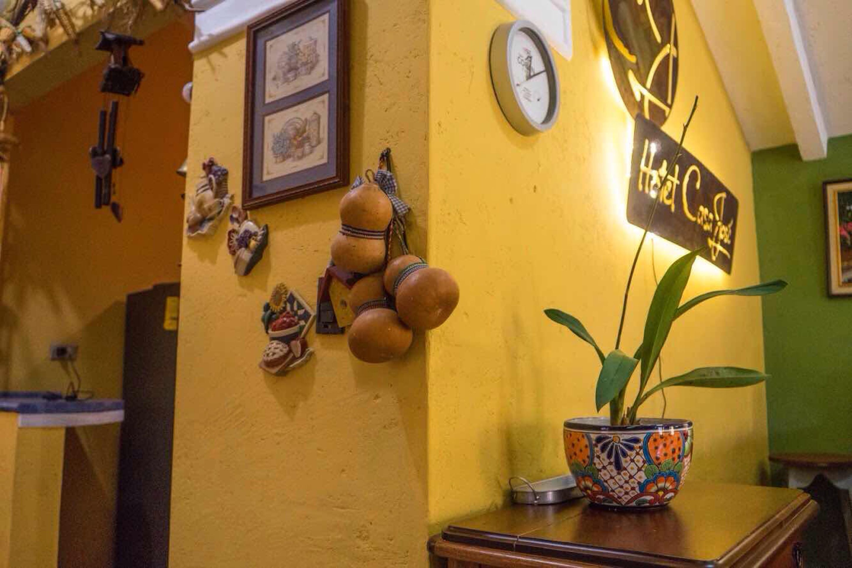 Un área de recepción con un reloj, un letrero que dice "Hot Coffee" y una planta en maceta sobre una mesa de madera.