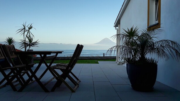 A patio with a table and chairs, a potted plant, and a view of the ocean and a mountain. - Casa d'Avó Guesthouse (Velas)