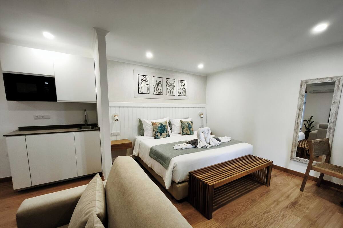 Una habitación de hotel moderna con una cama, un sofá, un banco de madera, un televisor y obras de arte en la pared.