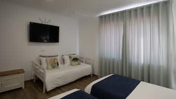 A bedroom with two beds, a flat-screen TV mounted on the wall, a bedside table, and a window with curtains.