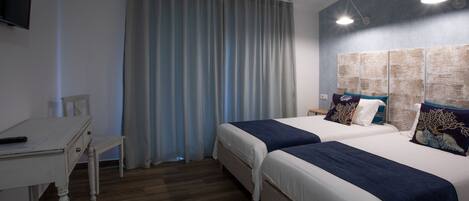 A hotel room with two beds, a desk, a TV, and a large window with curtains.