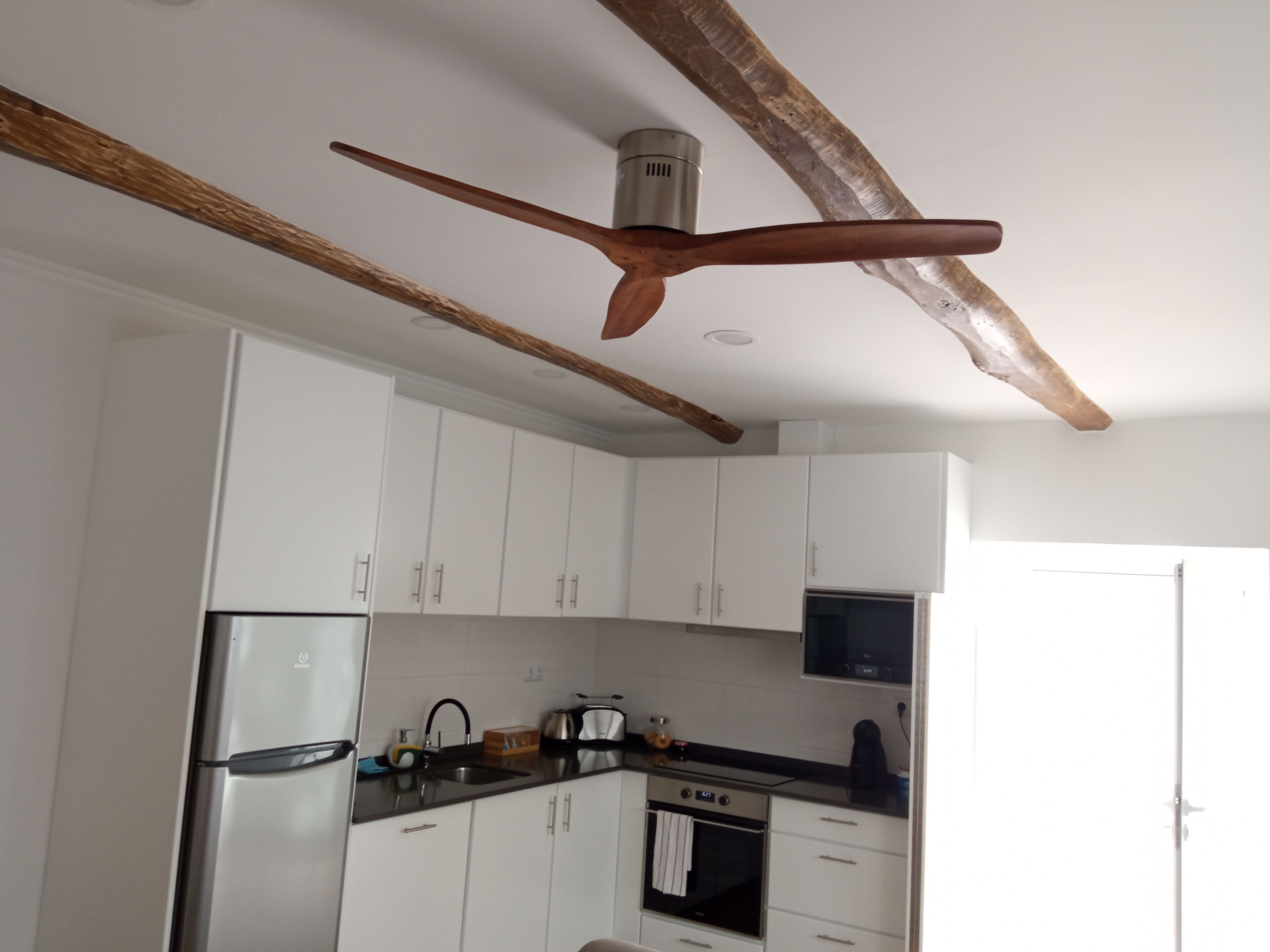 A modern kitchen with white cabinets, a stainless steel refrigerator, a built-in oven, and a ceiling fan.