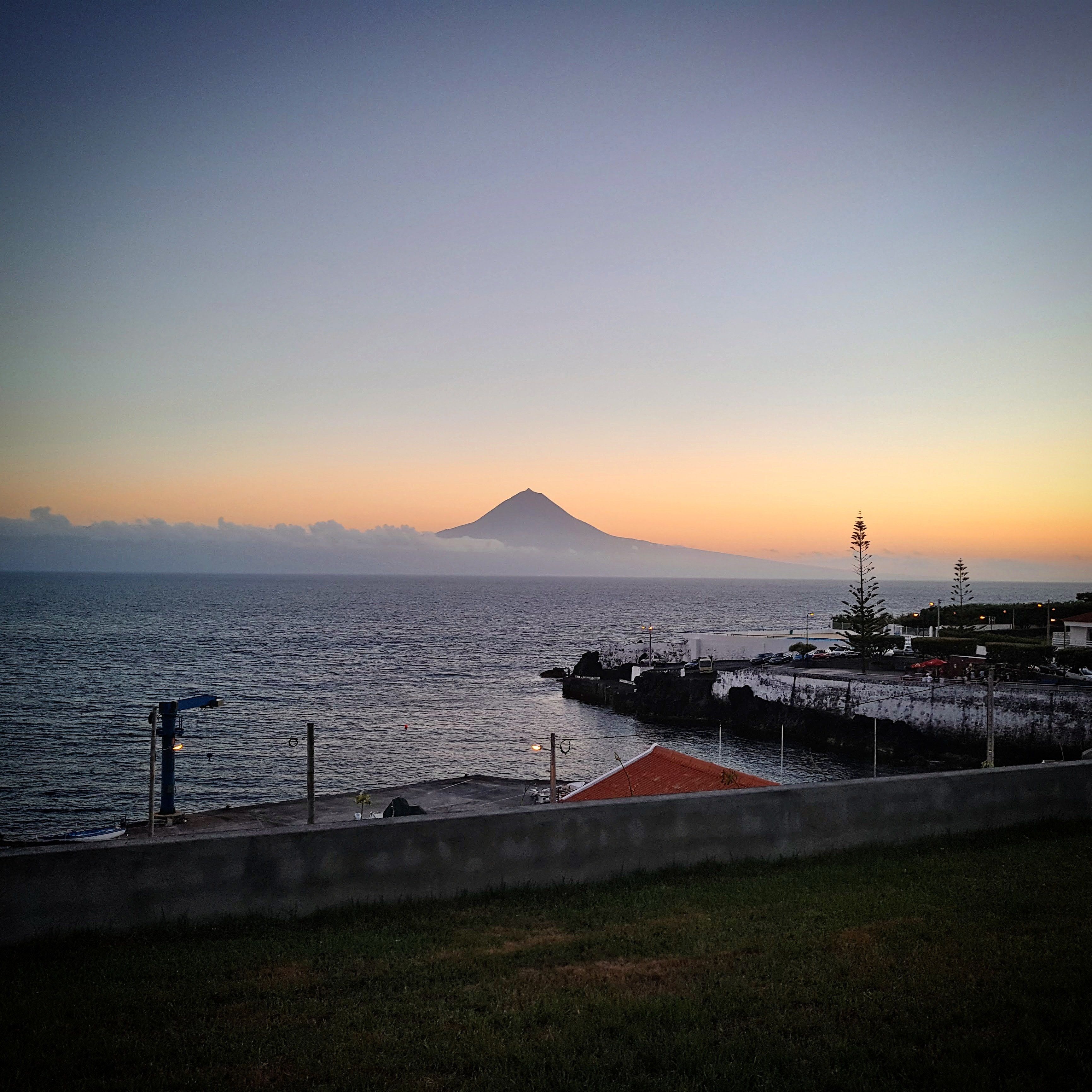 A coastal view with a mountain in the distance, a pier, and a grassy area.