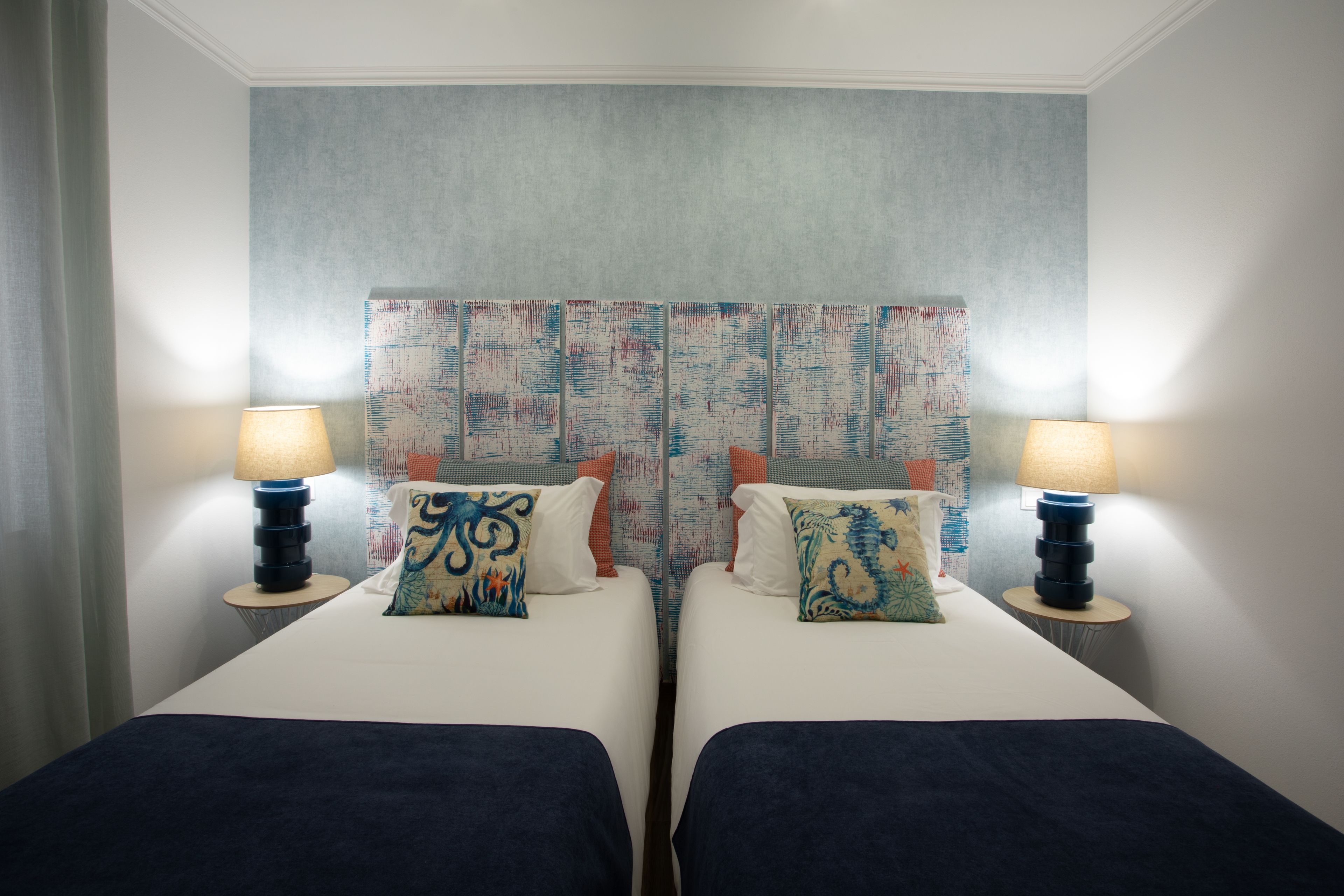 A hotel room with two beds, each with a lamp and decorative pillows.