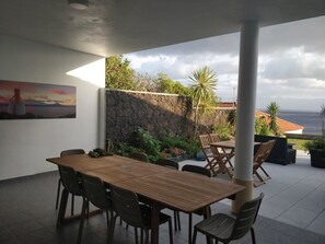 Eine Terrasse im Freien mit einem Holztisch und -stühlen, einer Steinmauer und Blick aufs Meer.