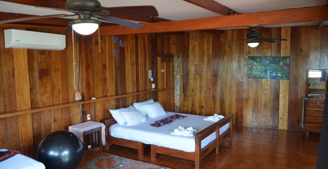 Een kamer met houten lambrisering, een bed, plafondventilatoren en een airconditioner.