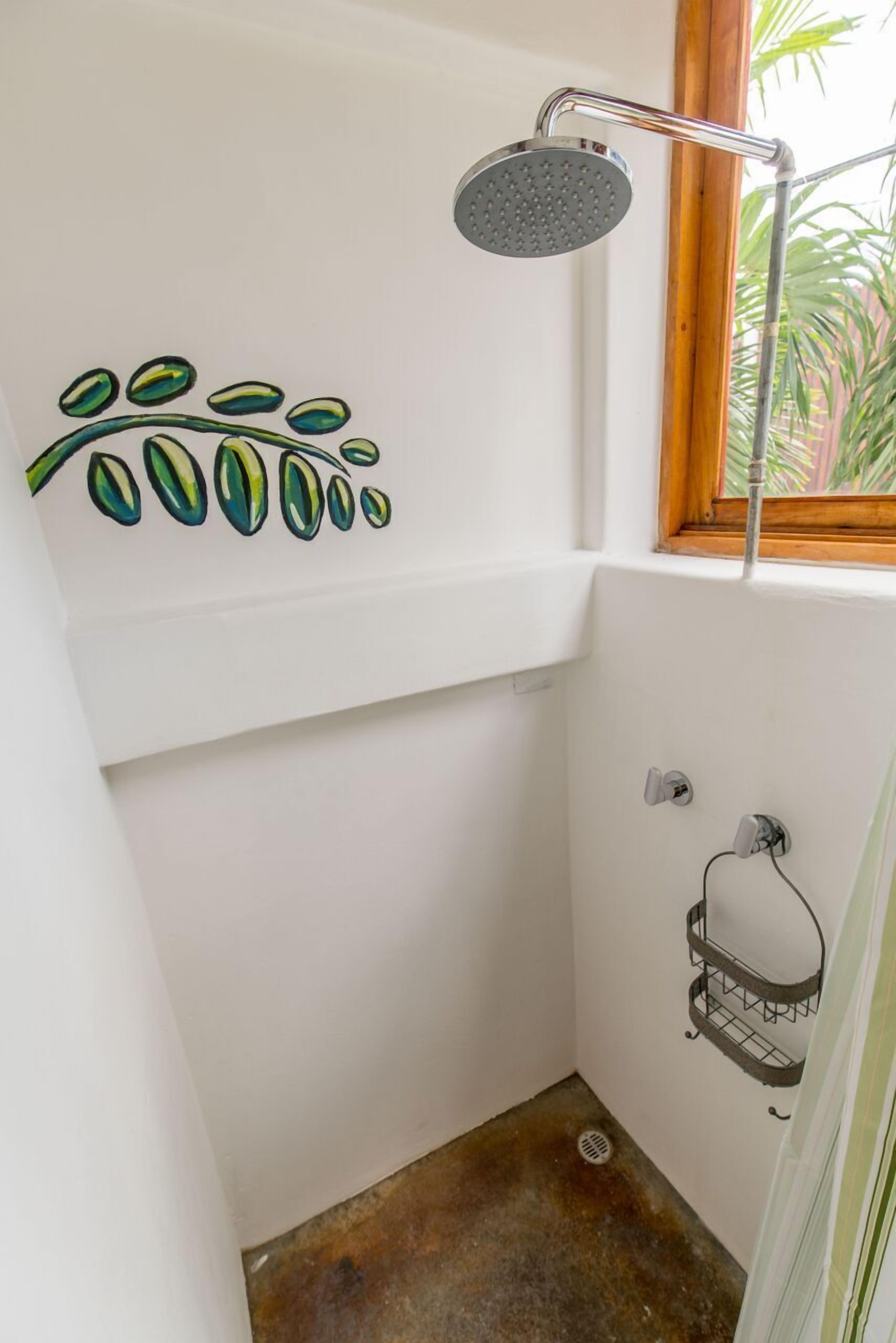A small, white bathroom with a shower, a window, and a wall-mounted shelf.