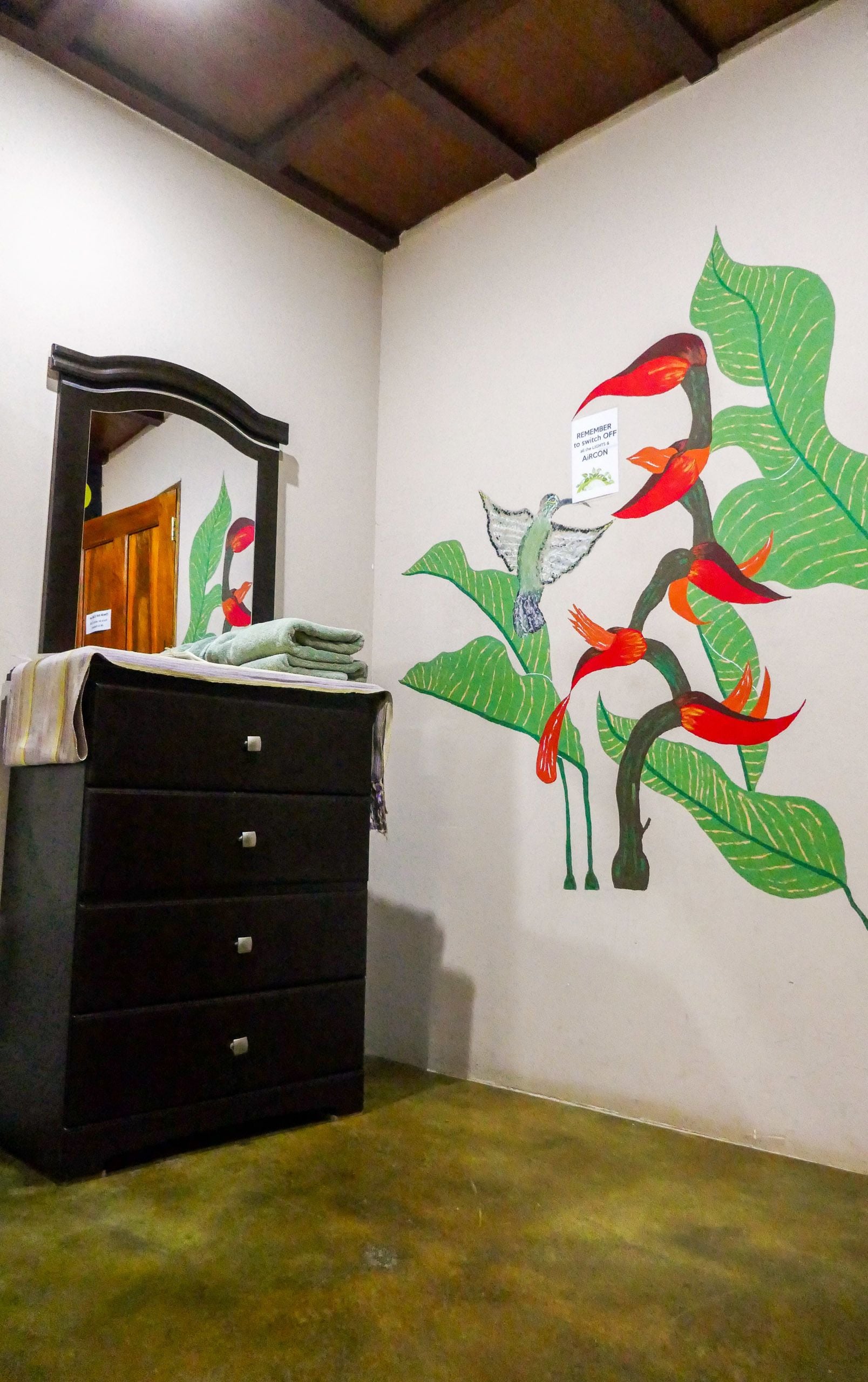 Una habitación con un aparador negro, un espejo y un mural en la pared que muestra un pájaro posado sobre una planta.