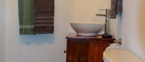 Un baño con inodoro blanco, un mueble de madera, lavamanos blanco y un espejo.