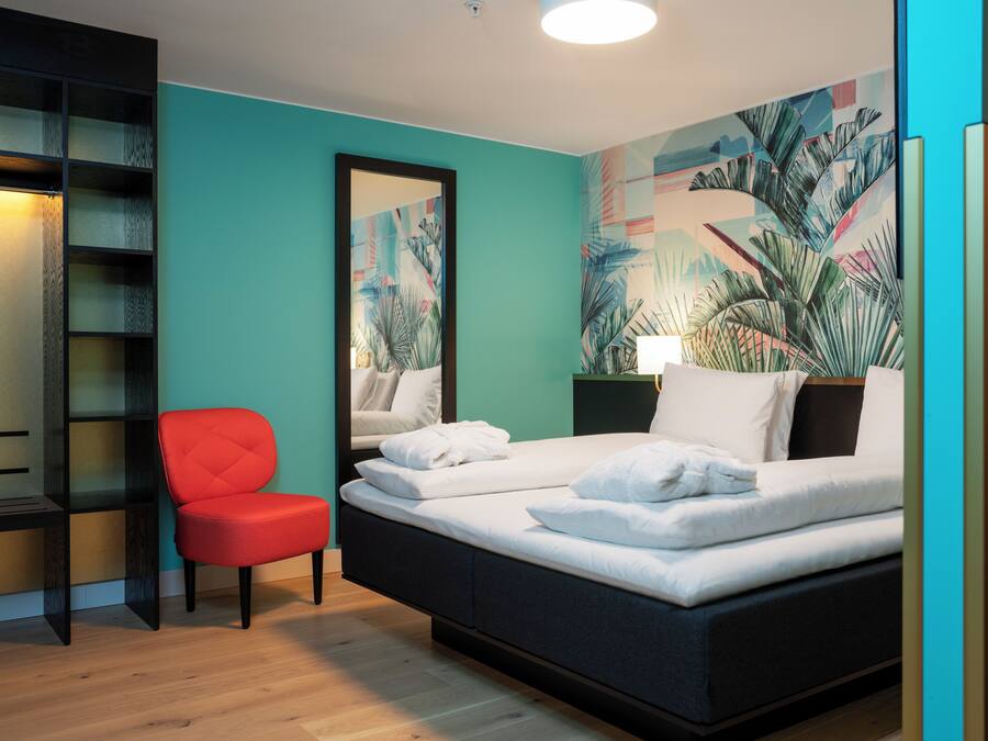 A bedroom with a bed, a red chair, a bookshelf, and a large mirror.