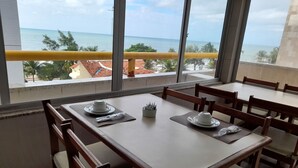 A dining area with a table set for two, overlooking a beach with palm trees and a clear sky. - Aquamar Praia Hotel (Recife)