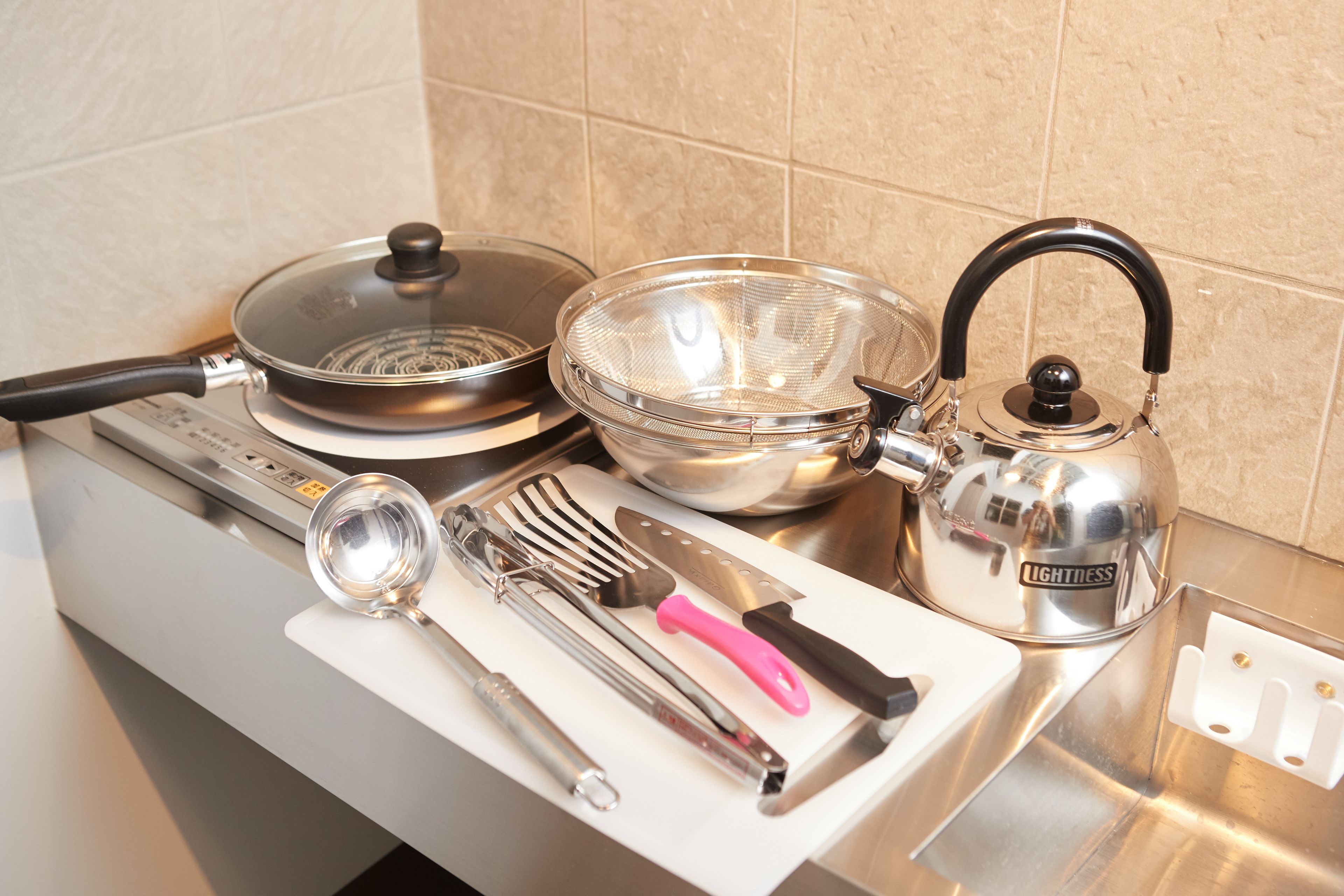 Un plan de travail de cuisine avec une cuisinière, une bouilloire, une poêle, une passoire, une spatule et une louche.