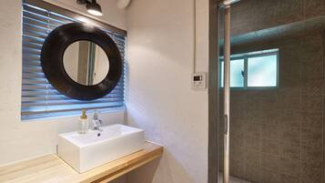 A bathroom with a white sink, a round mirror, and a shower area.