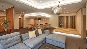 Una sala de estar moderna con un sofá seccional, un comedor con mesa y sillas de madera, y una cocina al fondo.