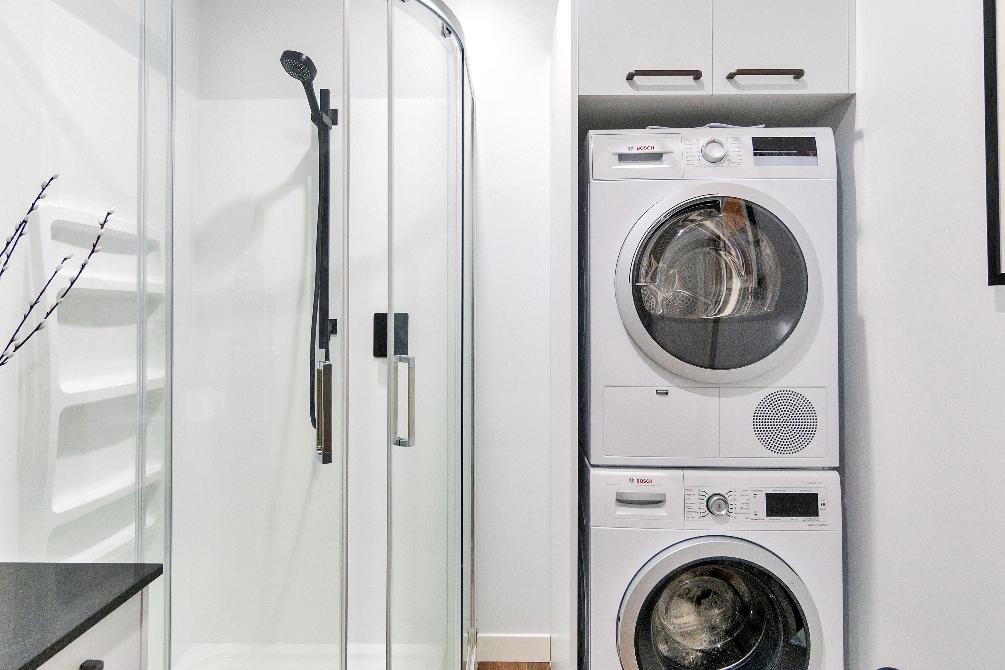 A modern laundry room with stacked Bosch washing machines and a glass shower enclosure.