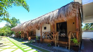 A thatched-roof building with a wooden deck, surrounded by potted plants and a stone pathway. - Allura Resort Dive and Spa (Zamboanguita)