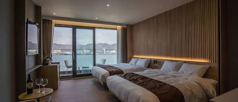 A modern hotel room with two beds, a dining area, and a view of the sea.