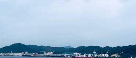 Zona costera industrial con barcos y grúas, probablemente un puerto o astillero, con montañas al fondo.