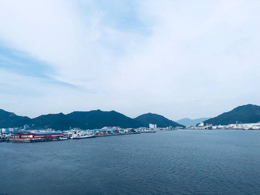 A coastal cityscape with a marina, mountains in the background, and a clear sky.