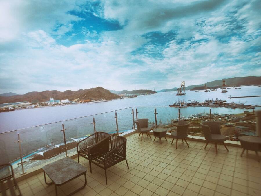 A terrace with chairs and tables overlooking a harbor with boats and a bridge.