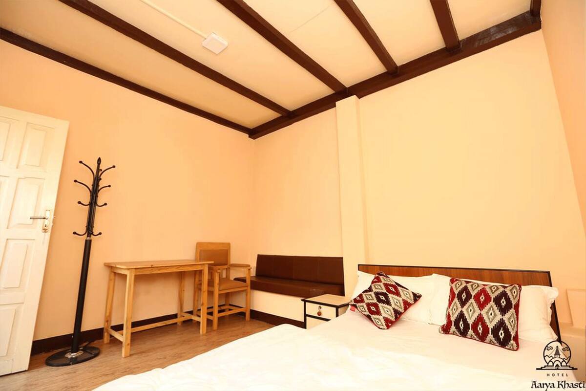 Une chambre à coucher comprenant un lit, un banc en bois, un porte-manteau et une petite table.