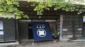 Perinteinen puurakennus, jonka edessä on suuri sininen banneri, jossa on japaninkielisiä merkkejä ja valkoinen tunnus.