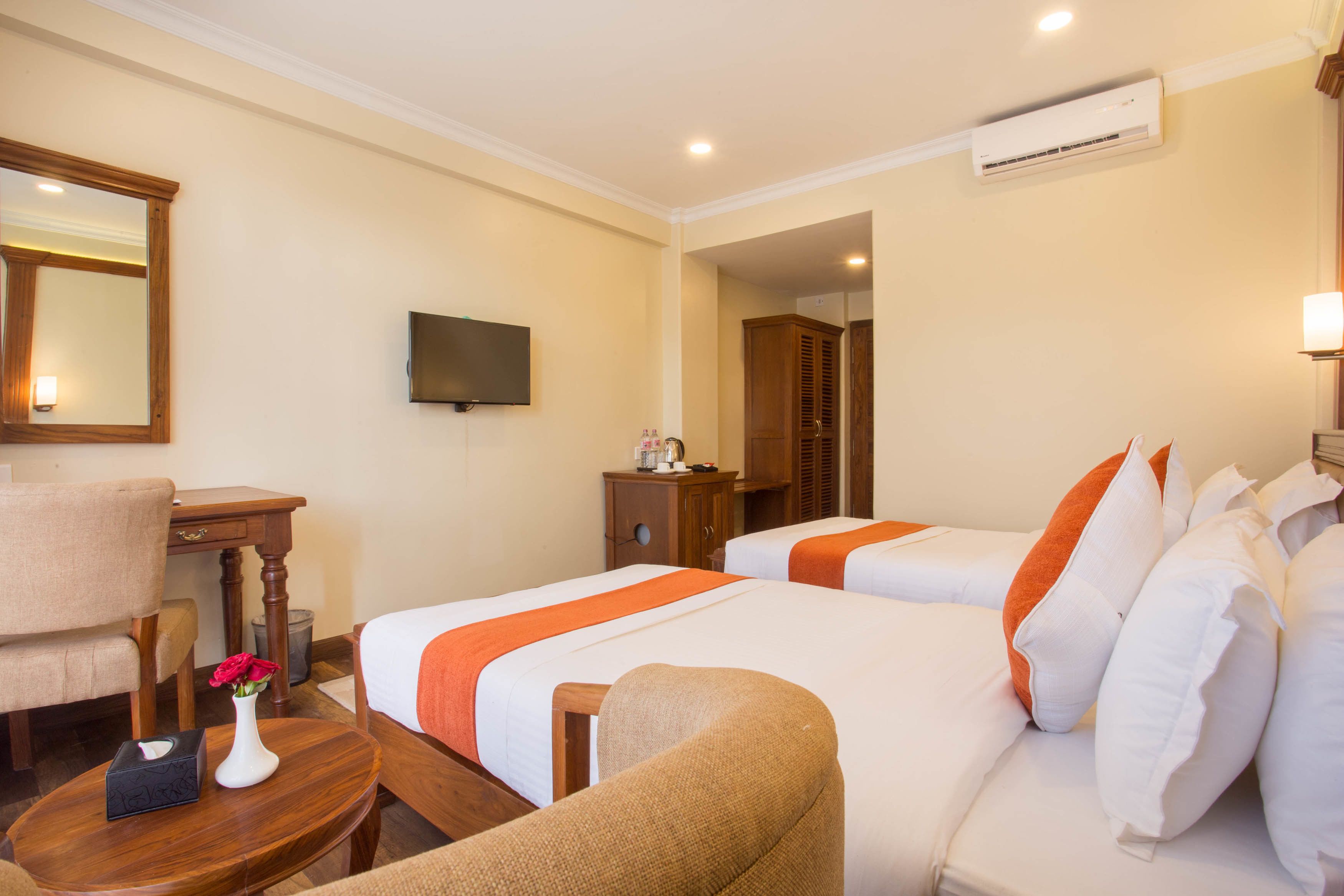 A hotel room with two beds, a desk, a chair, a TV, and an air conditioning unit.