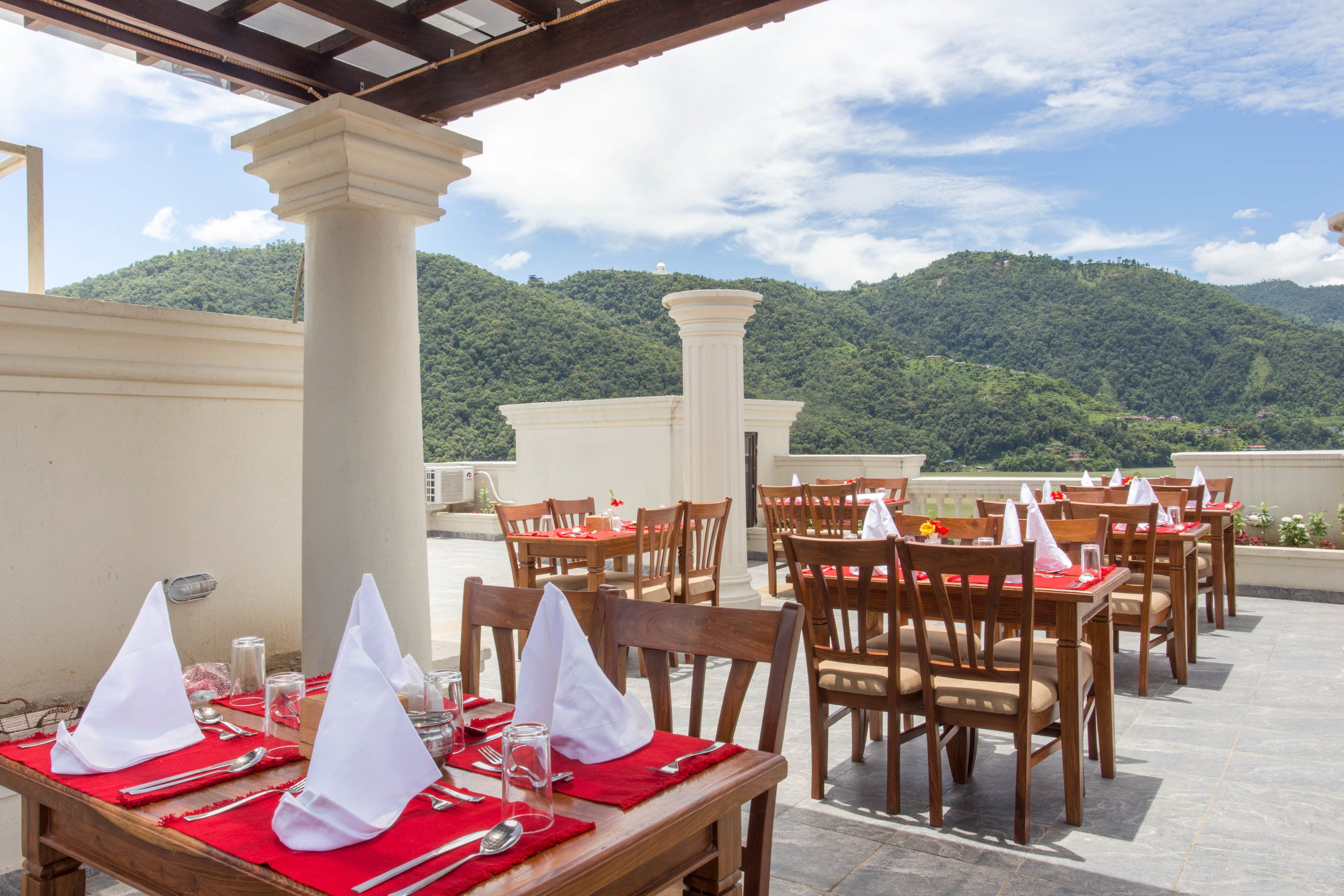 A rooftop dining area with tables set for two, featuring red tablecloths and white napkins.