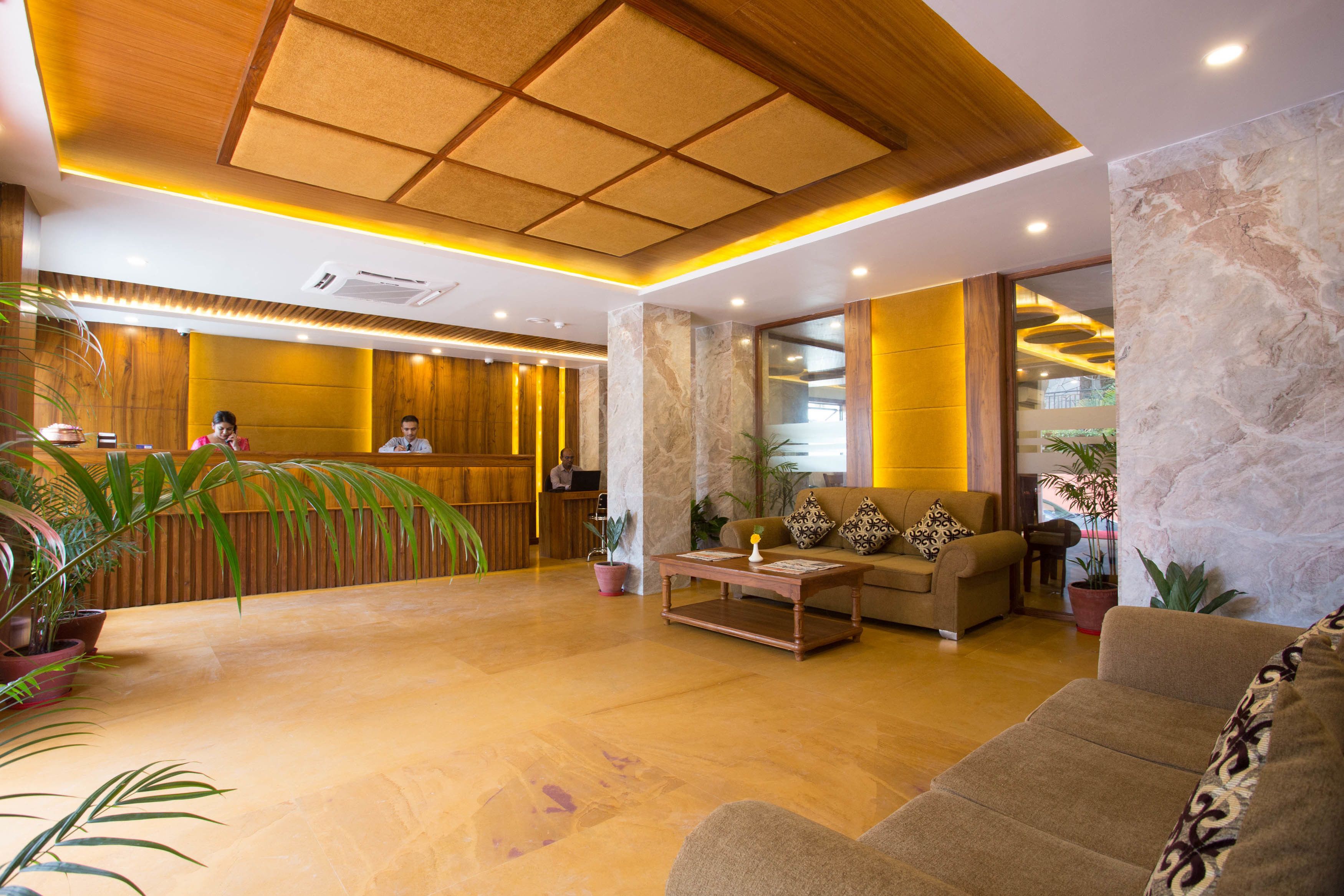 A hotel lobby with a reception desk, seating area, and potted plants.