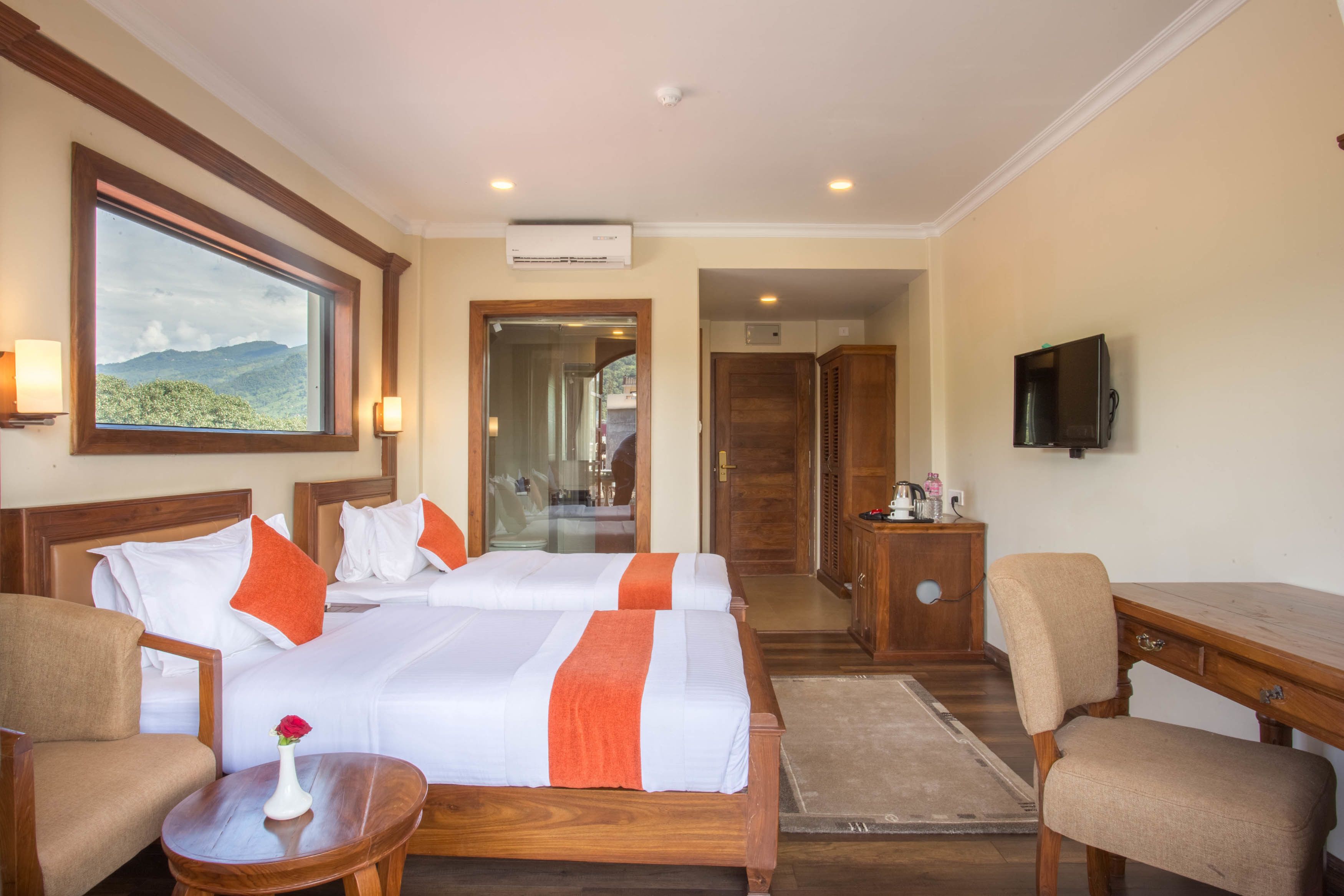 A hotel room with two beds, a TV, a desk, a chair, and a view of mountains.