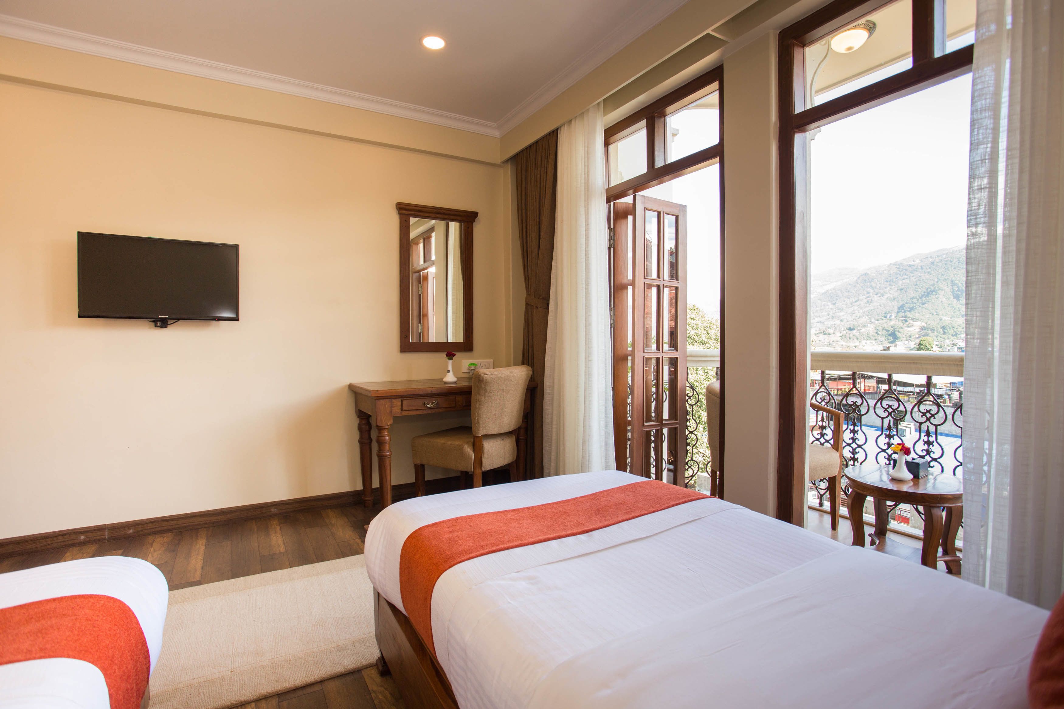 A hotel room with two beds, a desk, a chair, a TV, and a balcony with a view.
