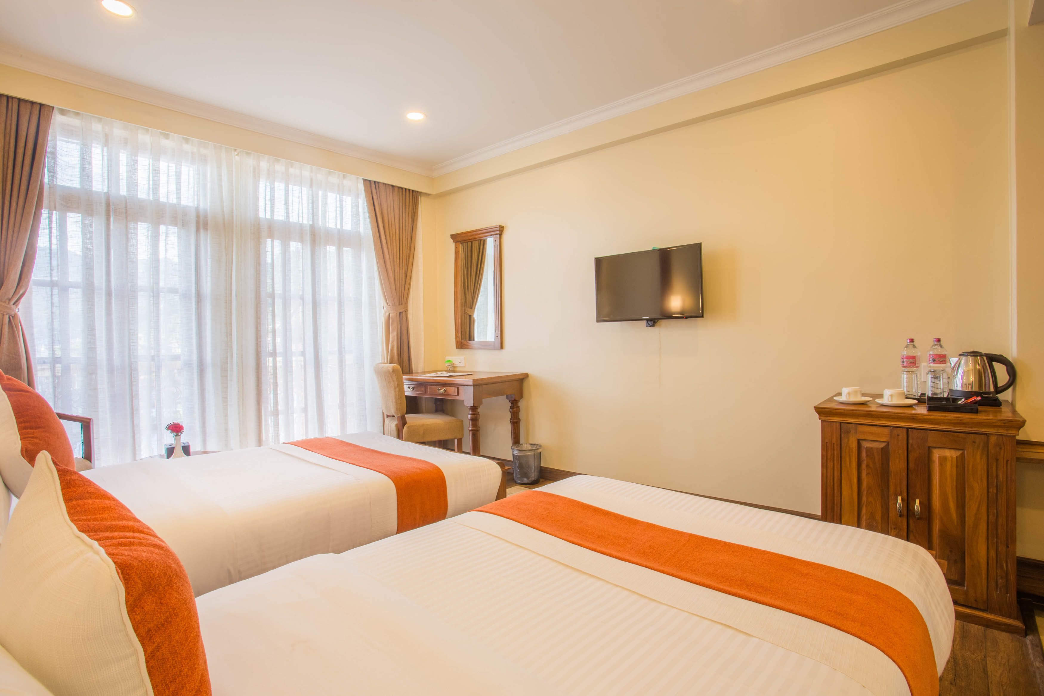 A hotel room with two beds, a desk, a television, and a cabinet with toiletries.