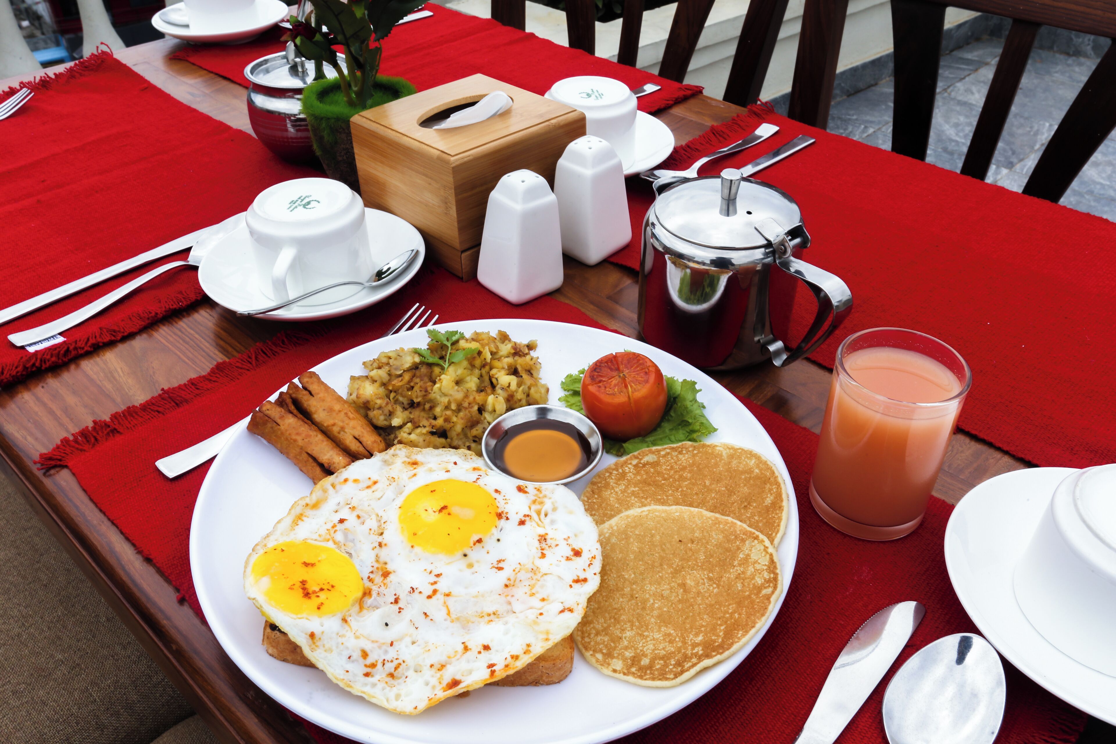 A breakfast plate with eggs, toast, and a glass of juice on a red tablecloth.