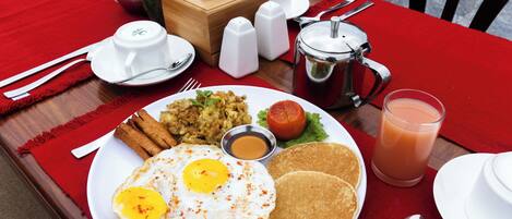 A breakfast plate with eggs, toast, and a glass of juice on a red tablecloth.