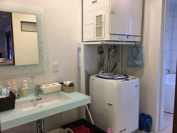 A bathroom with a white sink, mirror, and a white water heater. There are toiletries on the counter and a red towel on the floor. - Arimabaru Beach Resort (Motobu)