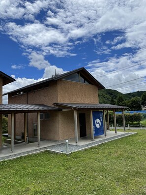 Um edifício moderno com área externa coberta, uma placa azul com texto branco e montanhas ao fundo.